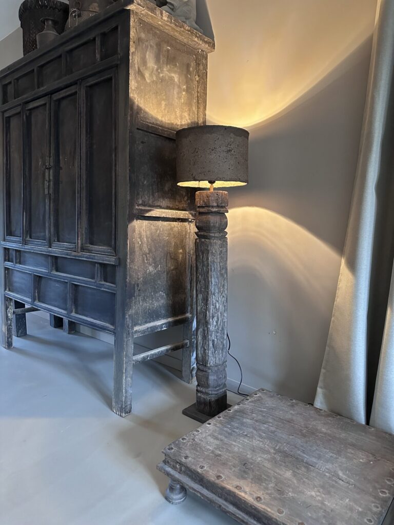 Deze unieke vloerlamp combineert de robuuste charme van historisch India met een organische, moderne afwerking. De voet van de lamp is vervaardigd uit een authentieke, oude houten pilaar uit India, waardoor elk exemplaar zijn eigen verhaal en unieke houtsnijwerk heeft. De lamp wordt gecompleteerd door een prachtige, handgemaakte leem lampenkap. Het natuurlijke materiaal van de kap zorgt voor een warme, sfeervolle lichtinval die direct rust en karakter in je woonkamer, hal of slaapkamer brengt. Specificaties: • Hoogte: 124,5 cm (ideale hoogte voor naast een bank of in een hoek) • Diameter kap: 30 cm • Materiaal voet: Antiek hout (originele Indiase pilaar) • Materiaal kap: Leem / Stuc-look • Stijl: Wabi-sabi, sober wonen, landelijk, industrieel of bohemien Belangrijke informatie: Vanwege de kwetsbaarheid van de leemkap en het gewicht van de antieke pilaar kan deze lamp niet verzonden worden. De lamp is uitsluitend op te halen in onze showroom/winkel.